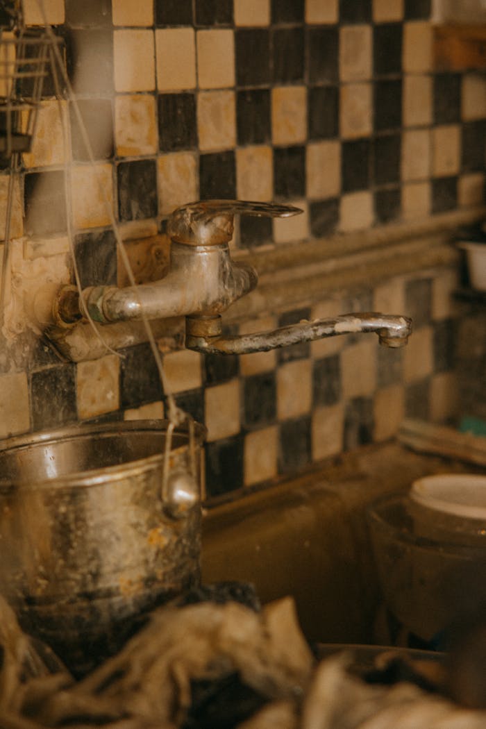 Close-up of a rusty kitchen faucet with stained tiles, showcasing neglect and wear.